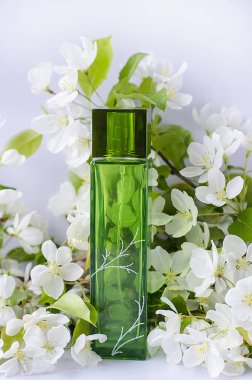 Parfüm, tuvalet suyu, arka planda yeşil şişe beyaz arka planda bir elma ağacının beyaz çiçekleri. Kozmetik reklamları için. Yatay fotoğraf 