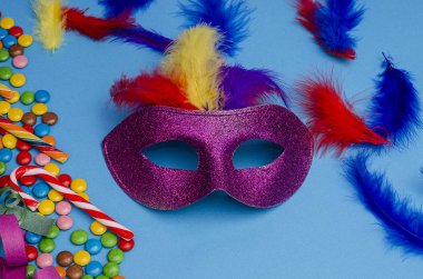 Karnaval. Şenlik arka planı. Karnaval maskesi mor, mavi arka planda tüyleri var. Süslü, çok renkli şekerleri var. Mardi Gras 'da. Brezilya Dili.