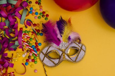 Karnaval. Şenlik arka planı. Sarı arka planda tüyleri olan karnaval maskesi. Süslü, balonlu, çok renkli şekerli. Mardi Gras 'da. Brezilya Dili.