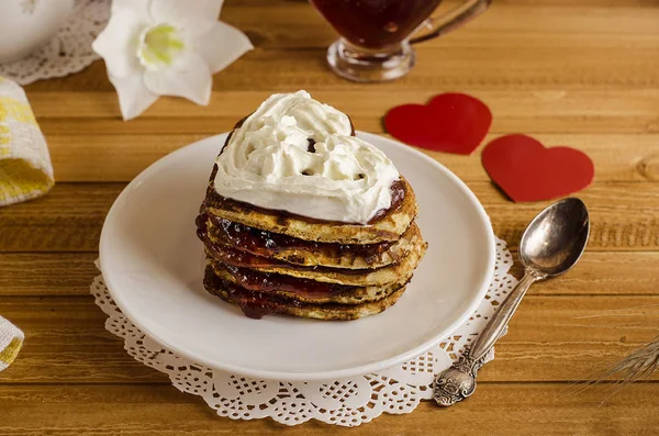 Fritters, pancakes in the form of hearts with jam and whipped cream on a light wooden background with a red heart, a romantic breakfast for Valentine's Day. Mothers Day. Cooking — Stock Photo, Image