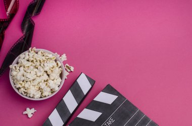 Patlamış mısır ve film şeritli el çırpma tahtası. Pembe arka planda fotokopi alanı var. Film hakkındaki makaleler için.. 