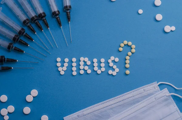 Tablets laid out with the word virus with a question mark and syringes on a light blue background. What are the symptoms of the virus? Issues of distribution and treatment.