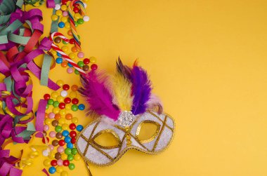 Karnaval. Şenlik arka planı. Sarı arka planda tüyleri olan karnaval maskesi. Süslü, kopya alanı olan çok renkli tatlılar. Mardi Gras 'da. Brezilyalı. Venedik.