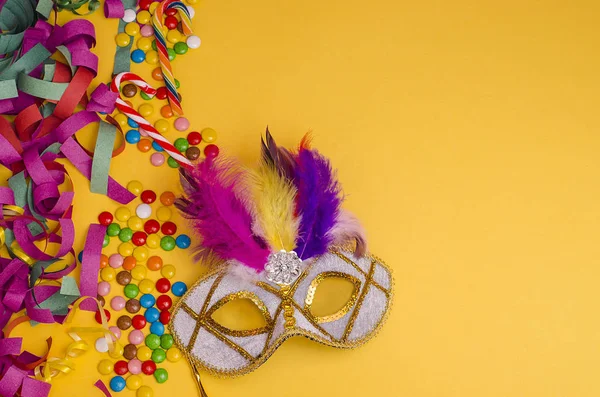 Karnaval. Şenlik arka planı. Sarı arka planda tüyleri olan karnaval maskesi. Süslü, kopya alanı olan çok renkli tatlılar. Mardi Gras 'da. Brezilyalı. Venedik.