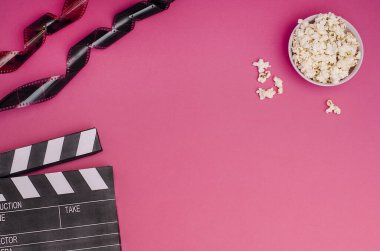 Patlamış mısır ve film şeritli el çırpma tahtası. Pembe arka planda fotokopi alanı var. Film hakkındaki makaleler için. Sinema kavramı.