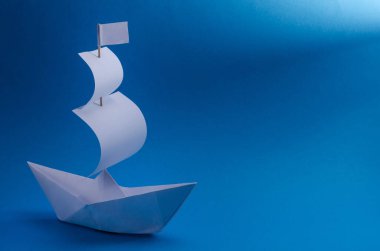 Mavi arka planda yelkenli beyaz kağıt tekne bir ışık demeti tarafından aydınlatılıyor, başarıya doğru ilerleme kavramı, yazın seyahat. Columbus Günü