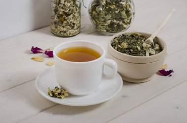 Beyaz ahşap bir masada bir fincan bitki çayı ve kurutulmuş bitkiler. Bağışıklığı arttırmak için, sağlık için doğal bir ilaç. Doğanın armağanları.