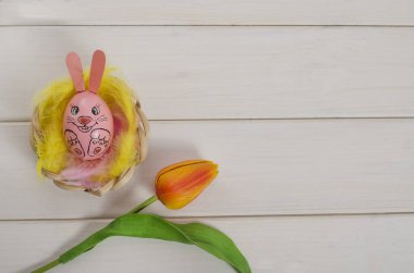 Paskalya kartı geçmişi. Beyaz ahşap arka planda tavşan şeklinde bir Paskalya yumurtası ve kopya uzayı olan tüyler. Mutlu Paskalyalar. Düz yatıyordu.