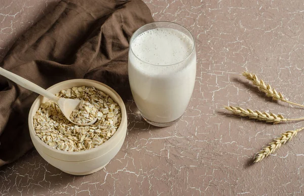 Oat milk in a glass on a beige background with oats, spikelets. The concept of veganism, raw food diet, healthy eating. Proper breakfast, children's menu.
