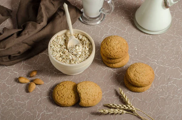 Oatmeal cookies on a beige background with oatmeal, spikelets and milk. The concept of veganism, healthy eating. Proper breakfast, children\'s menu. Homemade baking.