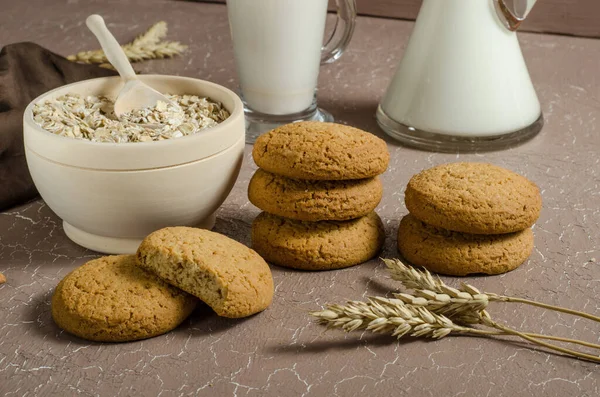 Oatmeal cookies on a beige background with oatmeal, spikelets and milk. The concept of veganism, healthy eating. Proper breakfast, children\'s menu. Homemade baking.