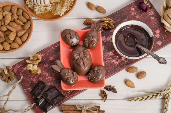 Chocolate Easter eggs in the form of a rabbit and chicken on a wooden white background with melted chocolate and nuts. Preparing for Easter. Happy easter.