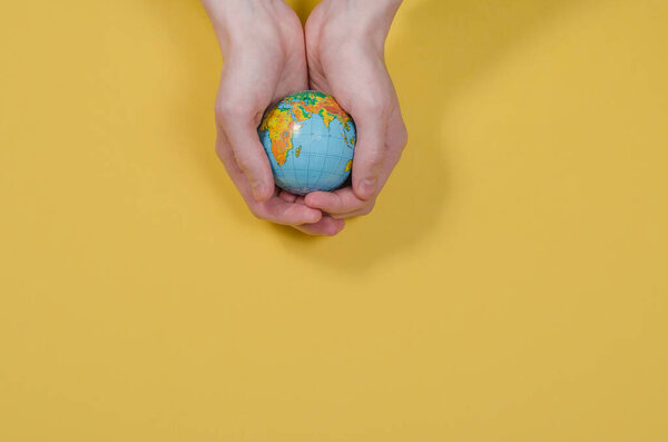 Globe in hands on a yellow background with copy space. The whole world is in your hands. Protect the world from war and disaster. Ecology problems.