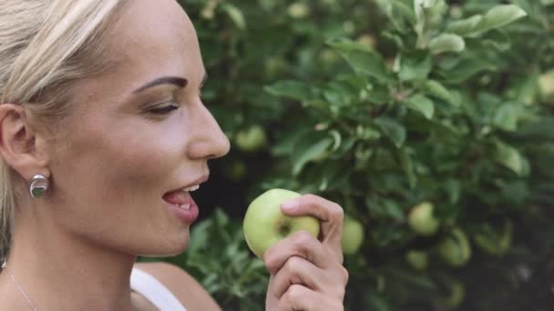 漂亮的金发姑娘咬下一个绿色的苹果 在镜头前眨眼 — 图库视频影像