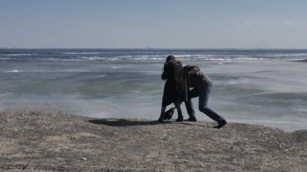 黒い帽子をかぶった若い男と女の子が川のほとりを歩いていて 氷に覆われていて 手をつないでいて 晴れた春の日には — ストック動画