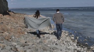 Genç çift, buzla kaplı bir nehrin yakınındaki kayalık bir sahilde yürüyor. Güneşli bir bahar günü.