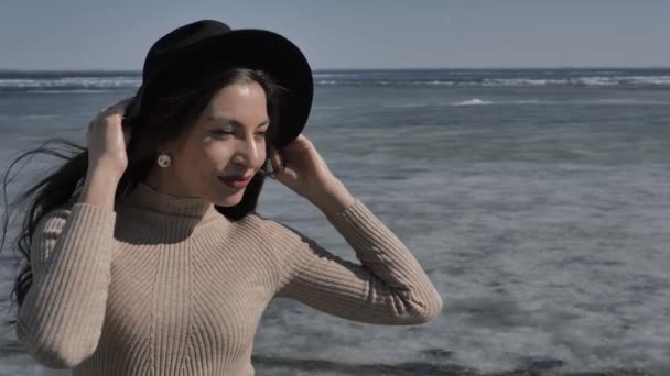 黒の帽子の若い美しい女の子は カメラと笑顔で 背景に氷で覆われた川 晴れた春の日に見えます — ストック動画