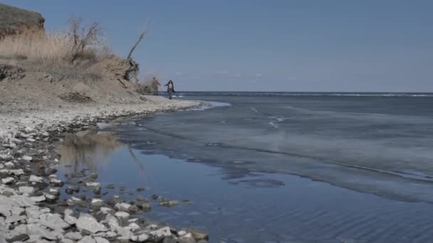 Pareja Joven Camina Largo Orilla Rocosa Del Río Cubierta Hielo — Vídeo de stock