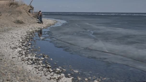 Pareja Joven Camina Largo Orilla Rocosa Del Río Cubierta Hielo — Vídeos de Stock