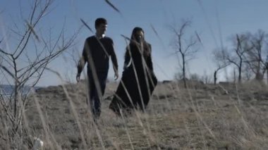 Young couple dressed in dark walks along the seashore, sunny day.