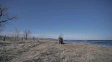 Young couple dressed in dark walks along the seashore, sunny day.