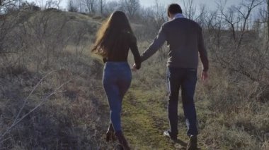 Young couple climbs a hill holding hands, sunny spring day.