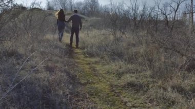 Young couple climbs a hill holding hands, sunny spring day.