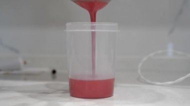 Kadın elleri plastik bir silindire kırmızı sıvı döker, yakın plan..