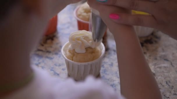 石のカウンターにはいくつかのカップケーキがあり お母さんは子供にクリームで飾る方法を示しています — ストック動画
