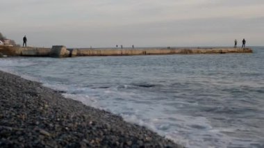 Denizde beton bir yapının üzerinde duran balıkçı ve turistlerin manzarası dalgalar kayalık sahile vurdu..