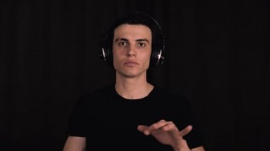Siyahlı ve kulaklıklı beyaz adam, kameranın önünde dans eden ve müzik dinleyen siyah arka planda, portre.
