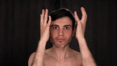 Beyaz bir adam, siyah bir arka planda, kameranın önünde yüzünü komik gösteriyor..