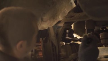 Asyalı bir adam atölyedeki asansörde kaldırılan eski bir arabanın şasesini tamir ediyor..