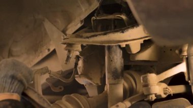 Asyalı bir adam atölyedeki asansörde kaldırılan eski bir arabanın şasesini tamir ediyor..