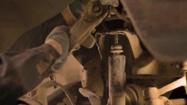 Asyalı bir adam atölyedeki asansörde kaldırılan eski bir arabanın şasesini tamir ediyor..