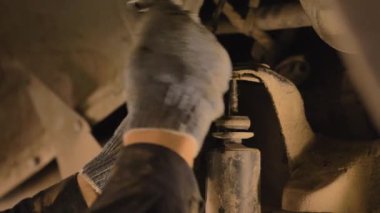 Asyalı bir adam atölyedeki asansörde kaldırılan eski bir arabanın şasesini tamir ediyor..