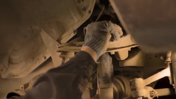 一名亚洲男子正在修理一辆旧车的底盘 这辆旧车是在一个车间的电梯上提起的 是个特写镜头 — 图库视频影像