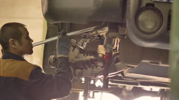 一名亚洲男子正在修理一辆旧车的底盘 这辆旧车是在一个车间的电梯上提起的 是个特写镜头 — 图库视频影像