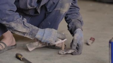 Eldivenli ve iş elbiseli Asyalı garajda yedek parça tamir ediyor, yakın plan..