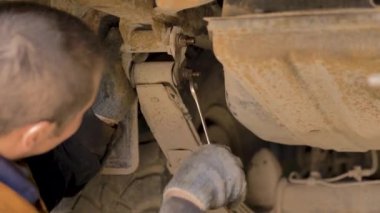 Asyalı bir adam atölyedeki asansörde kaldırılan eski bir arabanın şasesini tamir ediyor..