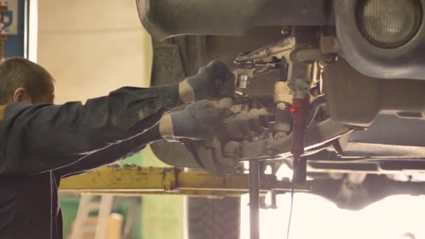 Un Asiatique est en train de réparer le châssis d'une vieille voiture soulevée sur un ascenseur dans un atelier, gros plan .