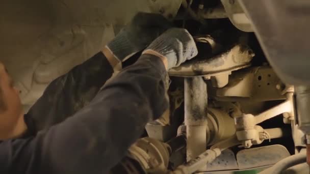 ワークショップでリフトで持ち上げられた古い車のシャーシを修理しているアジアの男 クローズアップ — ストック動画