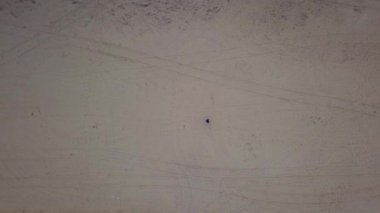 Bir adam kumlu bir arazide yürüyor, kumların üzerinde ayak izleri bırakıyor. Yukarıdan görüntüle.