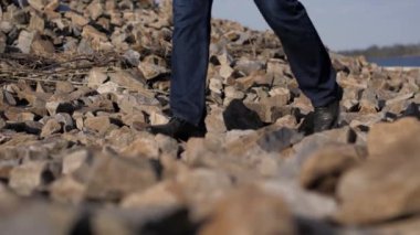 Erkeklerin bacakları taşların üzerinde yürür. Bir insanın yüzü görünmezdir. Güneşli yaz günü, açık havada.