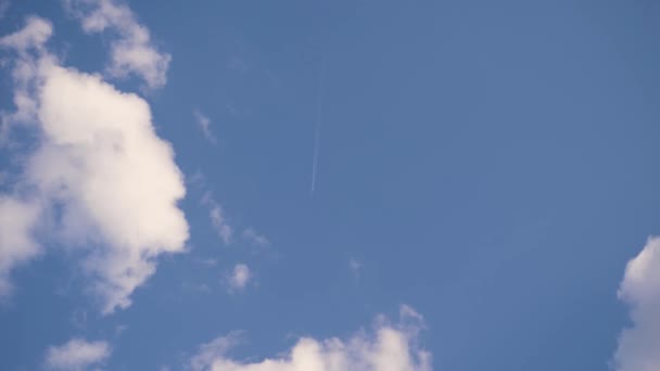 飛行機は遠くに飛び 白い縞模様が2本残されている 美しい青空と雲の背景を背景に 晴れた夏の日 路上で — ストック動画