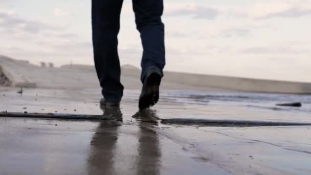 男性の足は川の岸に沿って歩く 地球のぬれた表面から反射が見える 夏の夜 — ストック動画