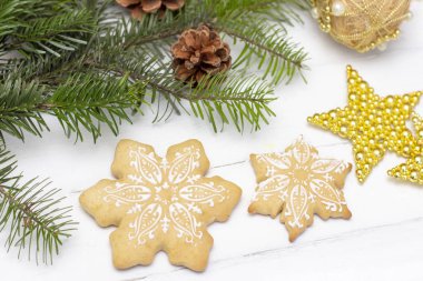 Noel kurabiyesi kar taneleri beyaz ahşap arka planda yatar. Arka planda Noel süslemeleri ve doğal ladin var..