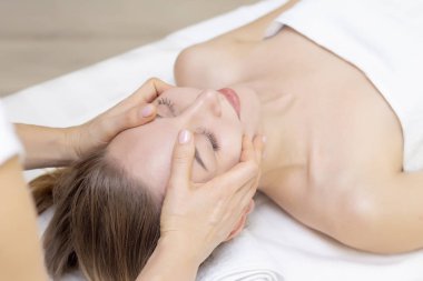 Genç bir kadın masaj salonundan zevk alıyor. Yüz masajı. Güzellik Salonu 'nda kaplıca masajı yaptıran genç bir kadın. Kaplıca ve vücut bakımı. Yüz güzelliği tedavisi. Kozmetoloji.. 