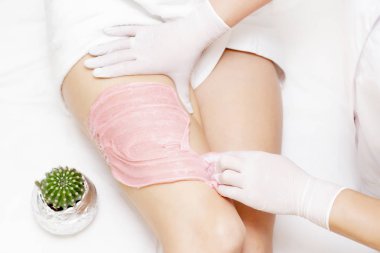 Shugaring ustasının elleri genç bir kızın kalçalarına pembe shugaring macunu sürerler. Arka planda bir kaktüs var. tükürük konsepti. Güzellik salonu spa merkezi.