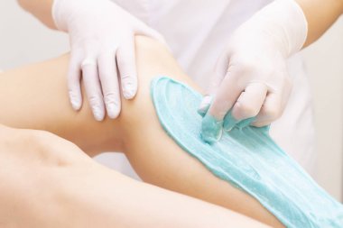 Güzellik uzmanı spa merkezinde sıvı şekerle genç kadınların bacaklarını tükürüyor. Turkuaz karıştırıcı macunla bacakların tükürüğü.
